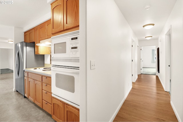 kitchen with under cabinet range hood, white appliances, light wood-style floors, light countertops, and baseboards