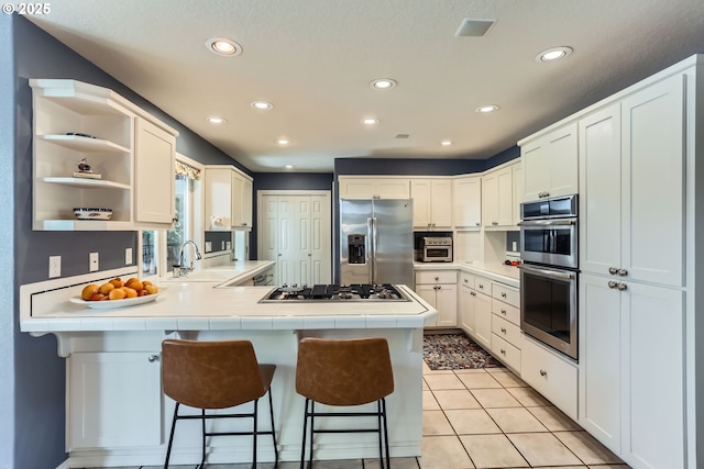 8650 SW Turquoise Loop, Beaverton, OR 97007 - kitchen featuring appliances with stainless steel finishes, a sink, a peninsula, tile counters, and a kitchen breakfast bar