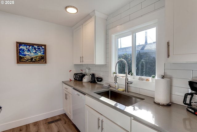 kitchen featuring tasteful backsplash, white cabinetry, sink, white dishwasher, and light hardwood / wood-style flooring