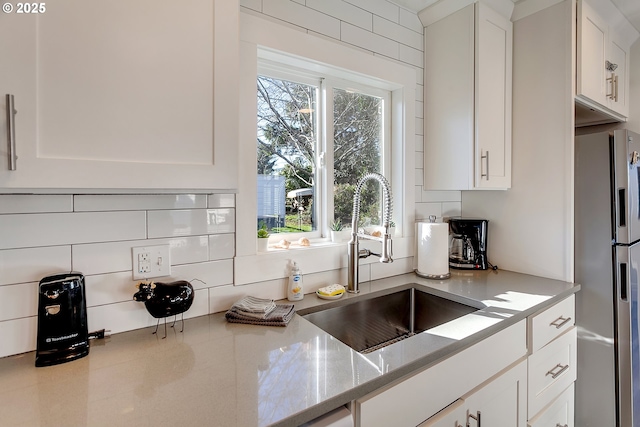 kitchen with sink, light stone counters, white cabinets, stainless steel fridge with ice dispenser, and decorative backsplash