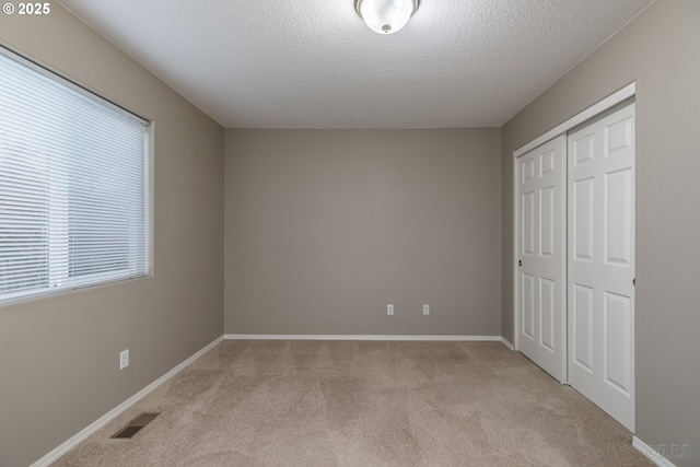 unfurnished bedroom featuring a textured ceiling, light colored carpet, visible vents, baseboards, and a closet