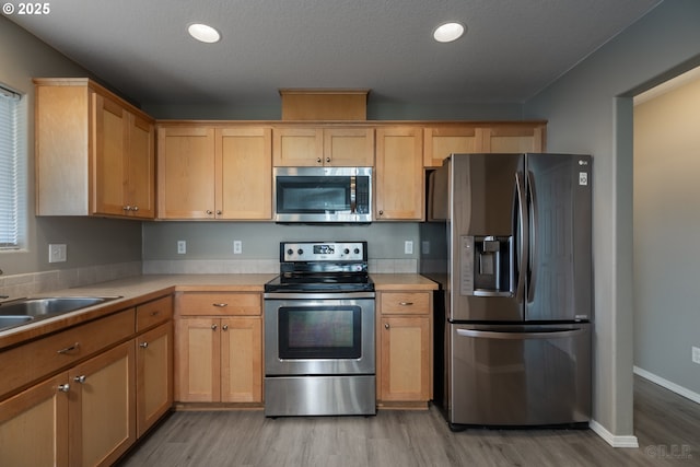 kitchen featuring light countertops, stainless steel appliances, a sink, and light wood-style floors