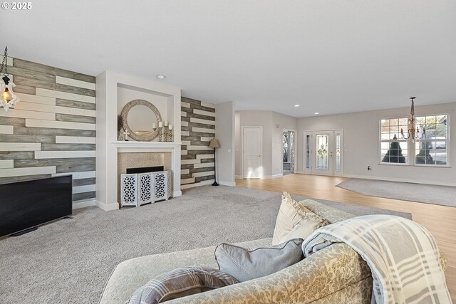 carpeted living room featuring a tiled fireplace, a notable chandelier, and wooden walls