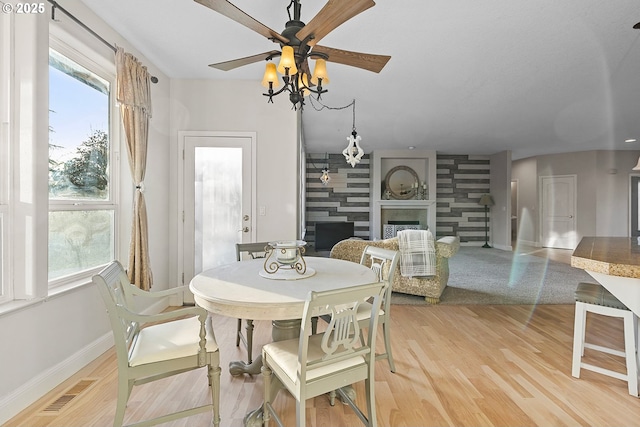 dining space featuring ceiling fan, a large fireplace, a healthy amount of sunlight, and hardwood / wood-style floors