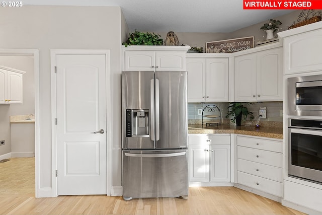 kitchen with tasteful backsplash, stainless steel appliances, light hardwood / wood-style flooring, and white cabinets