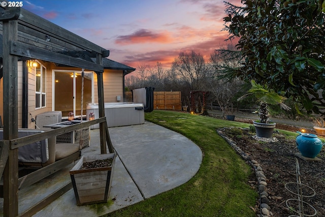 patio terrace at dusk featuring a hot tub and a lawn