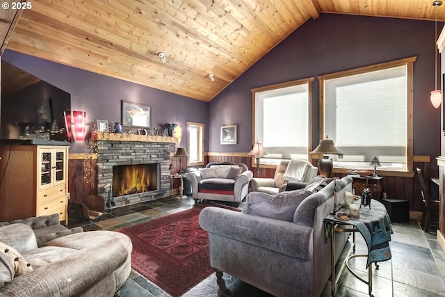 living room featuring vaulted ceiling, a wainscoted wall, stone tile flooring, a stone fireplace, and wood ceiling