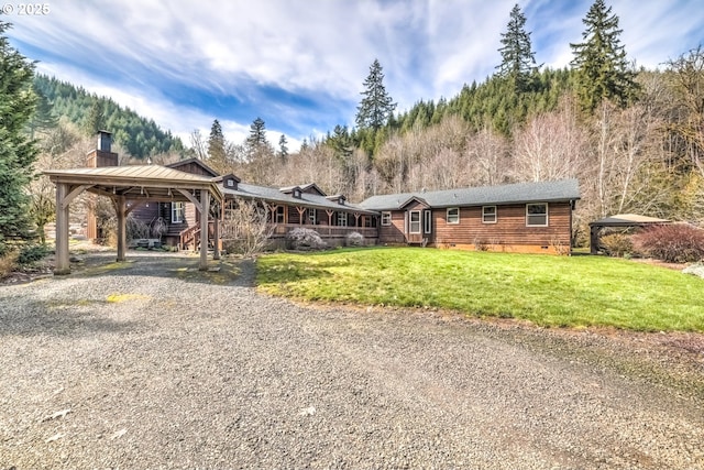 view of front facade featuring crawl space, a carport, a front lawn, a chimney, and gravel driveway