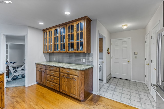 kitchen featuring light stone counters, light wood-type flooring, washer / dryer, and tasteful backsplash