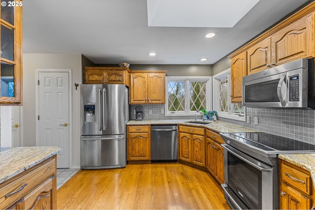 kitchen featuring backsplash, sink, a skylight, stainless steel appliances, and light stone counters