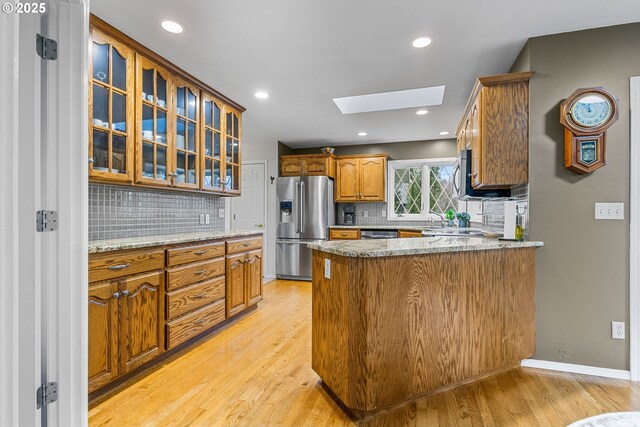 kitchen featuring appliances with stainless steel finishes, a skylight, sink, kitchen peninsula, and light hardwood / wood-style flooring