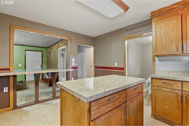 kitchen featuring tasteful backsplash, a center island, light tile patterned floors, and light stone counters