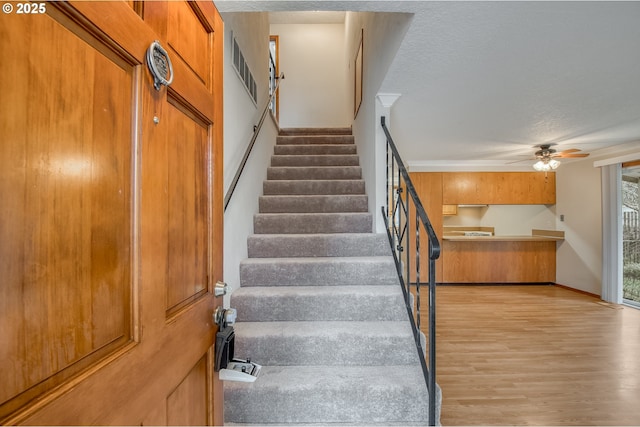 staircase with ceiling fan, wood-type flooring, and a textured ceiling