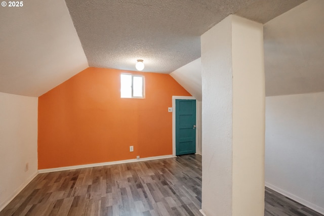 additional living space with dark wood-type flooring, lofted ceiling, and a textured ceiling