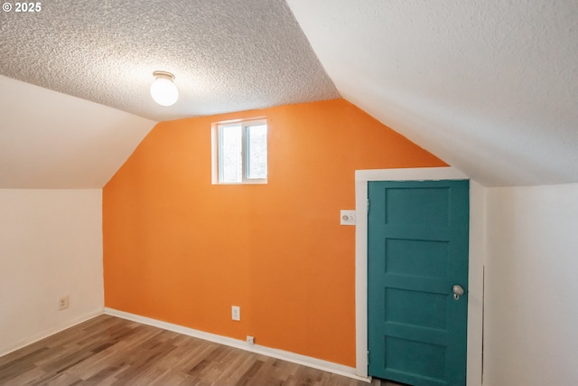 additional living space featuring hardwood / wood-style flooring, lofted ceiling, and a textured ceiling