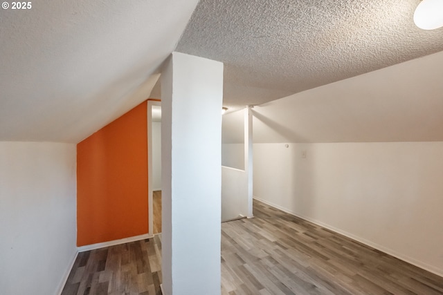 additional living space featuring lofted ceiling, hardwood / wood-style floors, and a textured ceiling