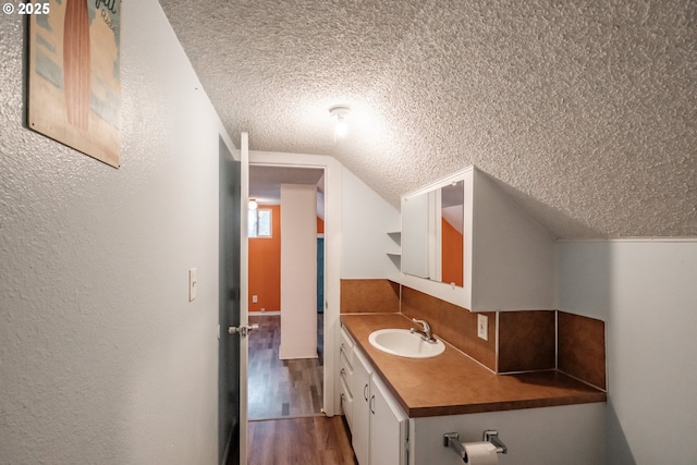 bathroom featuring wood-type flooring, vaulted ceiling, vanity, and a textured ceiling