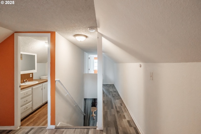 hall featuring vaulted ceiling, sink, a textured ceiling, and light hardwood / wood-style flooring