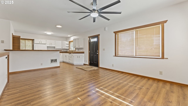 unfurnished living room with visible vents, light wood-style floors, ceiling fan, a sink, and baseboards