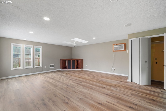 unfurnished living room with baseboards, a skylight, a wall mounted AC, and light wood-style floors