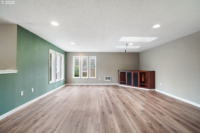 unfurnished living room with a textured ceiling, a skylight, baseboards, and wood finished floors