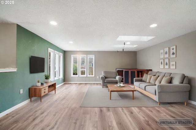 living area featuring a textured ceiling, a skylight, baseboards, and wood finished floors