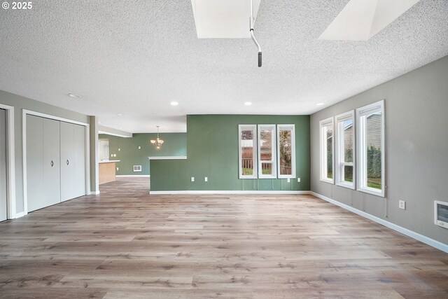 unfurnished living room featuring a chandelier, baseboards, visible vents, and wood finished floors