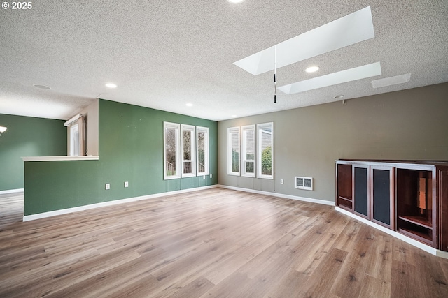 unfurnished living room with a textured ceiling, a skylight, baseboards, and wood finished floors