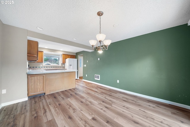 kitchen featuring a peninsula, baseboards, light wood finished floors, and a chandelier