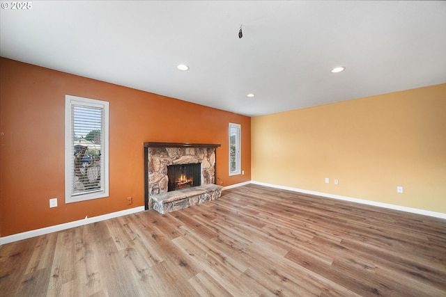 unfurnished living room with a stone fireplace, recessed lighting, baseboards, and wood finished floors
