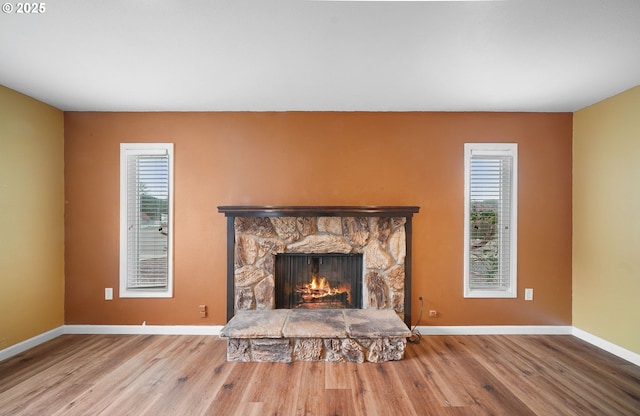 unfurnished living room featuring a stone fireplace, baseboards, and wood finished floors