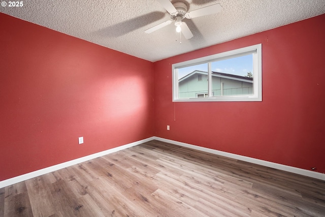 empty room with ceiling fan, a textured ceiling, baseboards, and wood finished floors