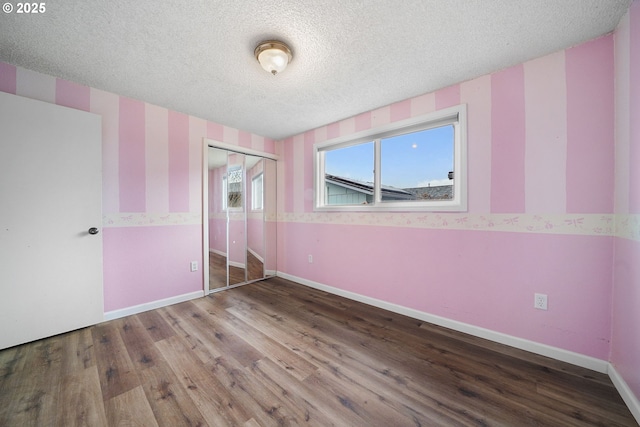 unfurnished bedroom with wallpapered walls, baseboards, wood finished floors, a closet, and a textured ceiling