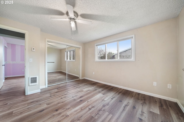 unfurnished bedroom with a textured ceiling, wood finished floors, a closet, and baseboards