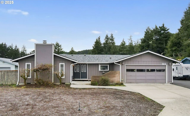 view of front facade with fence, an attached garage, a shingled roof, a chimney, and concrete driveway