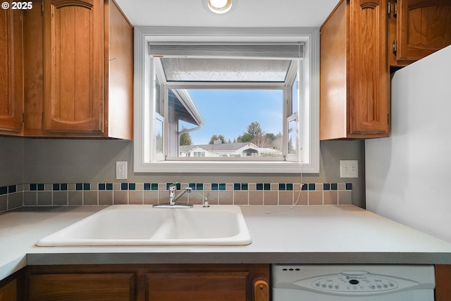 kitchen with brown cabinetry, dishwasher, light countertops, and a sink