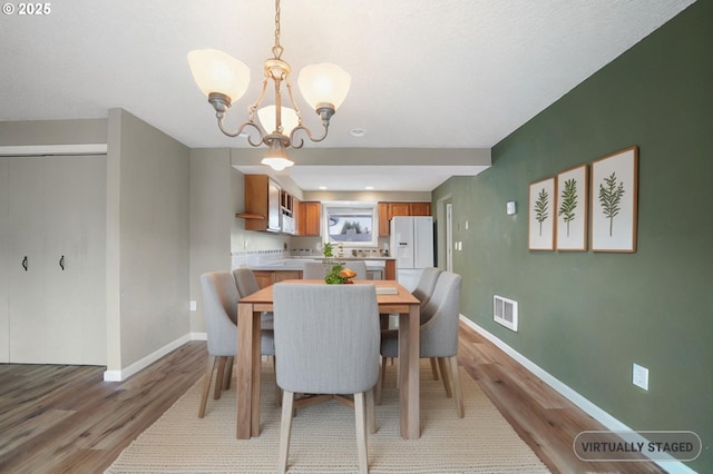 dining space featuring visible vents, baseboards, a notable chandelier, and light wood-style flooring