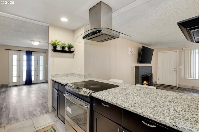 kitchen featuring light stone countertops, a lit fireplace, stainless steel electric range, island exhaust hood, and a textured ceiling