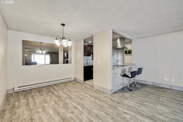 interior space with light wood-type flooring, a baseboard heating unit, a textured ceiling, baseboards, and a chandelier