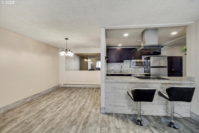 kitchen featuring wood finished floors, island exhaust hood, stainless steel appliances, a kitchen breakfast bar, and baseboard heating