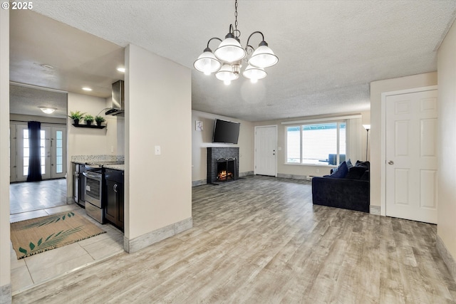 unfurnished living room with baseboards, a chandelier, a lit fireplace, light wood-style floors, and a textured ceiling