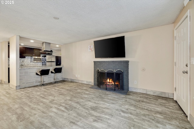 living area featuring a brick fireplace, a textured ceiling, baseboards, and wood finished floors