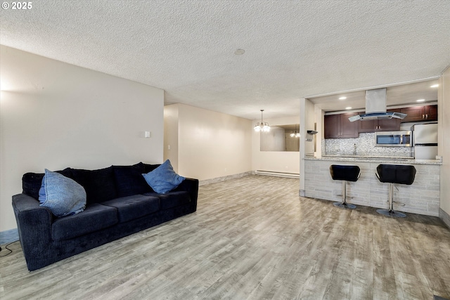 living room featuring baseboards, a baseboard radiator, an inviting chandelier, light wood-style flooring, and a textured ceiling