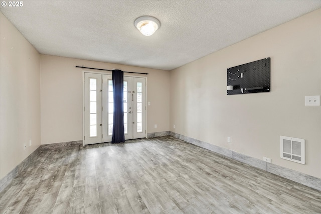 empty room featuring visible vents, baseboards, a textured ceiling, and wood finished floors