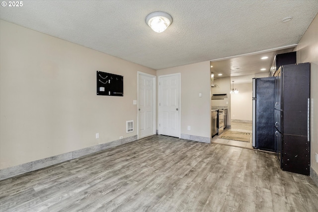 unfurnished living room with visible vents, baseboards, a textured ceiling, and light wood-style flooring