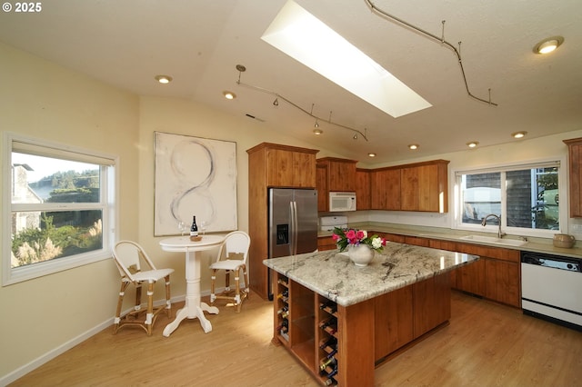 kitchen with light stone countertops, white appliances, a kitchen island, sink, and lofted ceiling with skylight