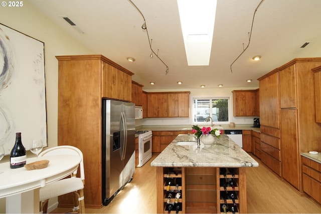 kitchen featuring white appliances, a kitchen island, a skylight, light hardwood / wood-style floors, and light stone counters