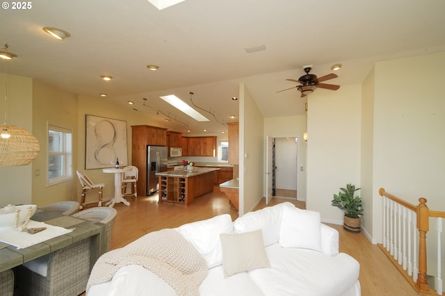 living room with ceiling fan, light wood-type flooring, and lofted ceiling with skylight