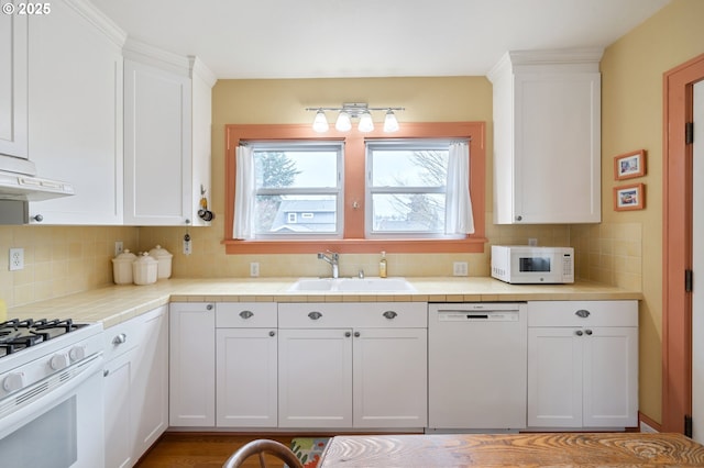 kitchen with a sink, backsplash, tile countertops, white appliances, and white cabinets