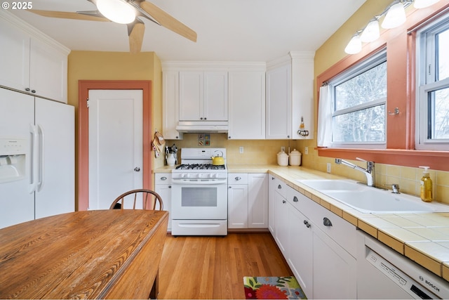 kitchen with white appliances, a sink, decorative backsplash, white cabinets, and under cabinet range hood